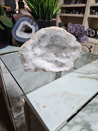Clear Quartz Geode crystal on a table with a plant.

CHIQUE Rock Shop