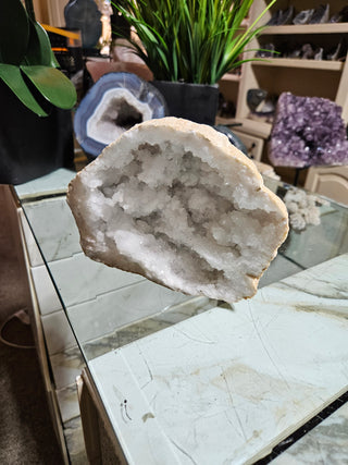 Clear Quartz Geode crystal on a table with a plant.

CHIQUE Rock Shop