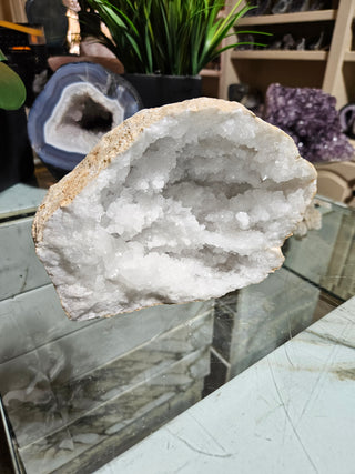 Clear Quartz Geode crystal on a table with a plant.

CHIQUE Rock Shop