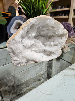 Clear Quartz Geode crystal on a table with a plant.

CHIQUE Rock Shop