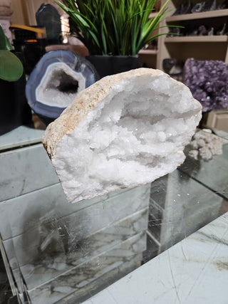 Clear Quartz Geode crystal on a table with a plant.

CHIQUE Rock Shop