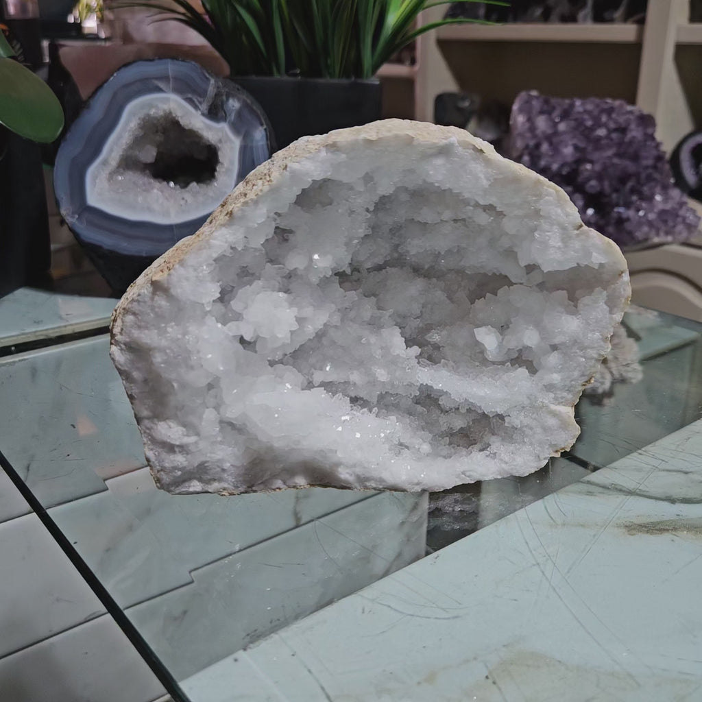 Clear Quartz Geode crystal on a table with a plant.

CHIQUE Rock Shop